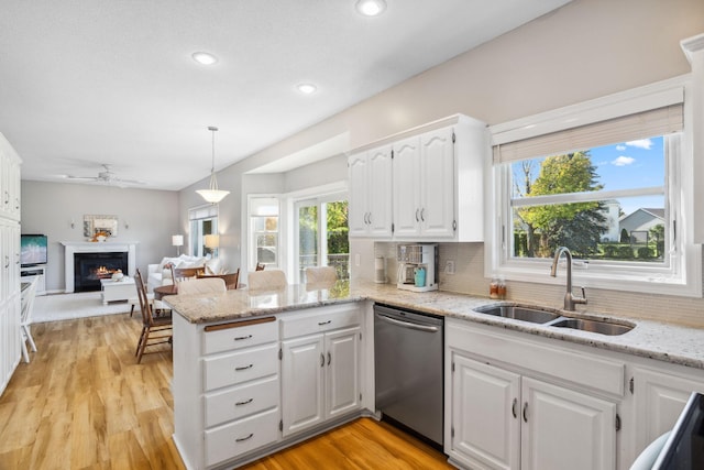 kitchen featuring a sink, a lit fireplace, a peninsula, white cabinets, and dishwasher