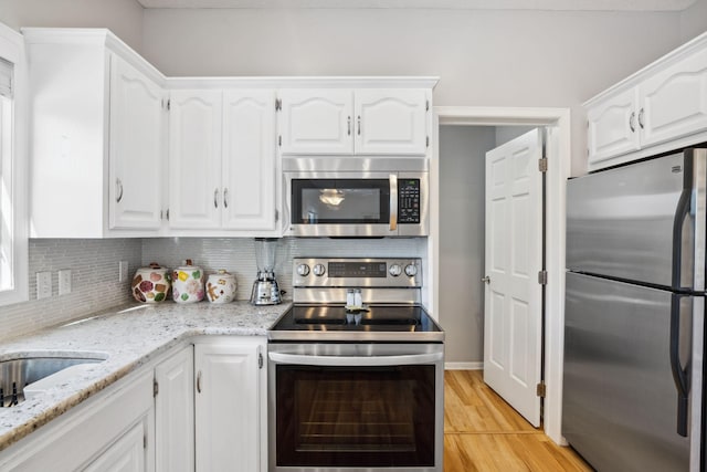 kitchen with white cabinetry, stainless steel appliances, light wood finished floors, decorative backsplash, and light stone countertops