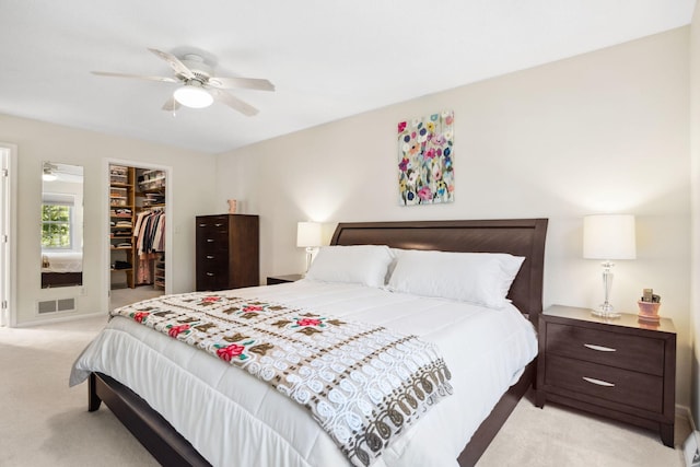 bedroom featuring a walk in closet, light carpet, visible vents, a ceiling fan, and a closet