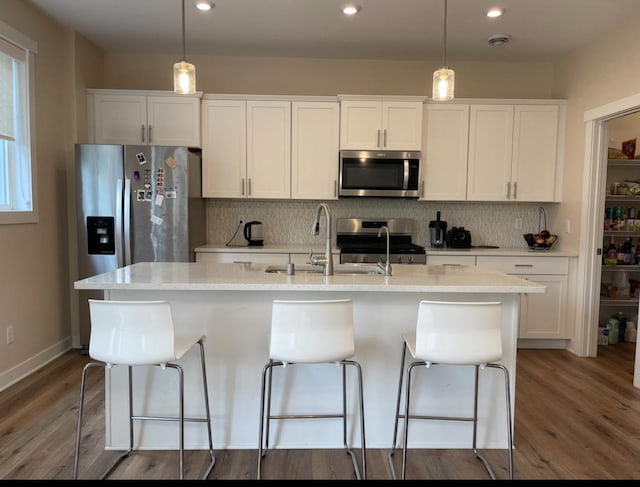 kitchen featuring white cabinets, stainless steel appliances, a center island with sink, and dark hardwood / wood-style flooring