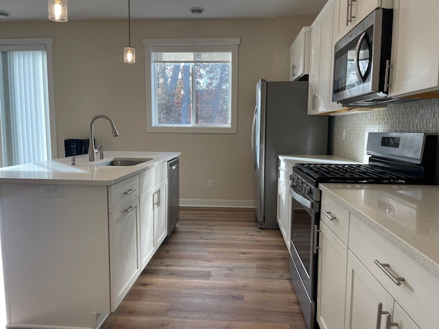 kitchen featuring wood-type flooring, hanging light fixtures, white cabinetry, stainless steel appliances, and a kitchen island with sink