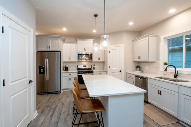 kitchen with light hardwood / wood-style flooring, a kitchen island, sink, decorative backsplash, and appliances with stainless steel finishes