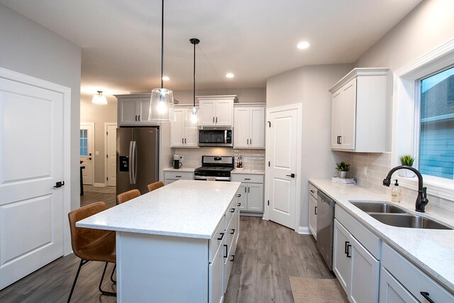 kitchen with hanging light fixtures, light hardwood / wood-style flooring, appliances with stainless steel finishes, sink, and a kitchen island