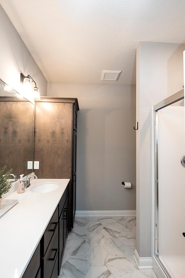 bathroom with a textured ceiling, vanity, and an enclosed shower