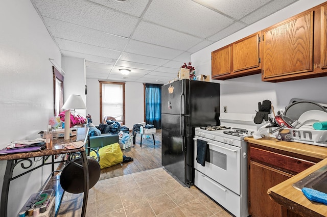 kitchen with black fridge, light hardwood / wood-style floors, a drop ceiling, and white gas stove