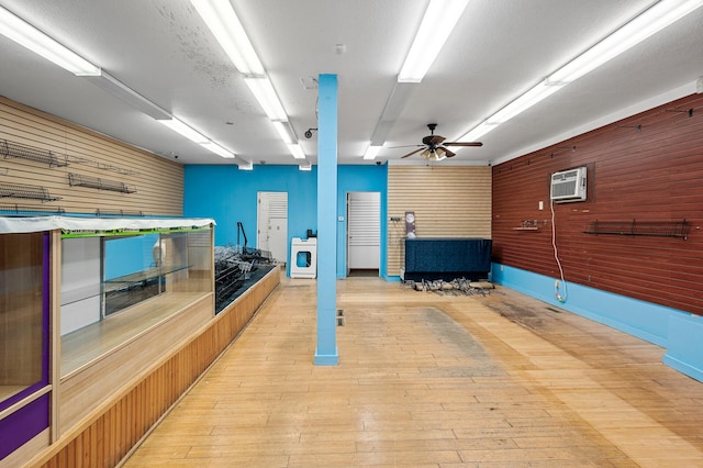 interior space featuring wood walls, light wood-type flooring, a textured ceiling, ceiling fan, and a wall mounted AC