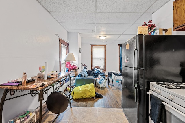 kitchen featuring hardwood / wood-style flooring, a drop ceiling, black refrigerator, and white range with gas stovetop