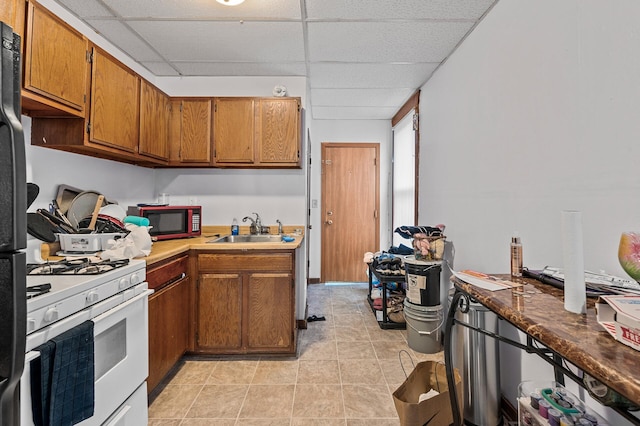 kitchen with a drop ceiling, black appliances, light tile patterned floors, and sink