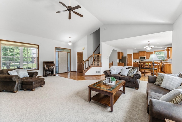 carpeted living room with high vaulted ceiling and ceiling fan with notable chandelier