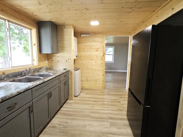 kitchen with wood walls, wooden ceiling, black fridge, sink, and light hardwood / wood-style floors