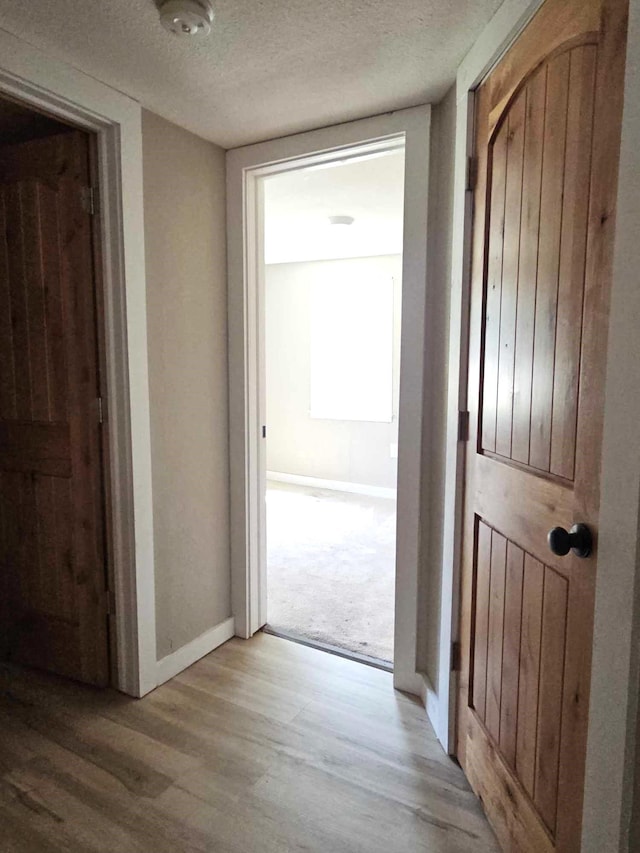 hallway with light wood-type flooring and a textured ceiling