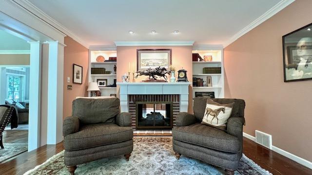 sitting room featuring ornamental molding, hardwood / wood-style floors, decorative columns, built in features, and a fireplace