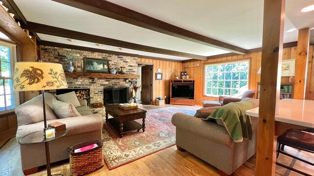 living room featuring beam ceiling, hardwood / wood-style flooring, a brick fireplace, and wooden walls