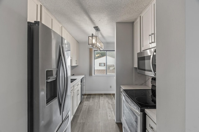 kitchen featuring wood-type flooring, decorative light fixtures, stainless steel appliances, and white cabinets