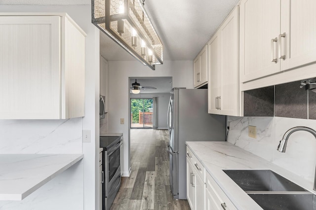 kitchen featuring appliances with stainless steel finishes, light stone countertops, dark hardwood / wood-style flooring, ceiling fan, and sink