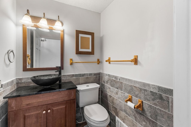 bathroom featuring a textured ceiling, tile walls, vanity, and toilet