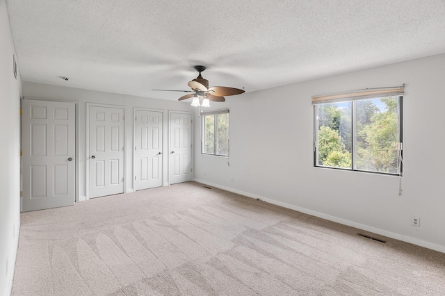 unfurnished bedroom with a textured ceiling, light carpet, two closets, and ceiling fan