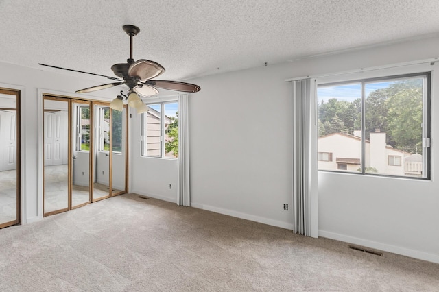 unfurnished bedroom with a textured ceiling, carpet flooring, two closets, and ceiling fan