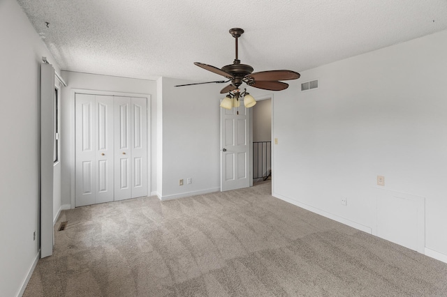 unfurnished bedroom featuring ceiling fan, a textured ceiling, a closet, and light carpet