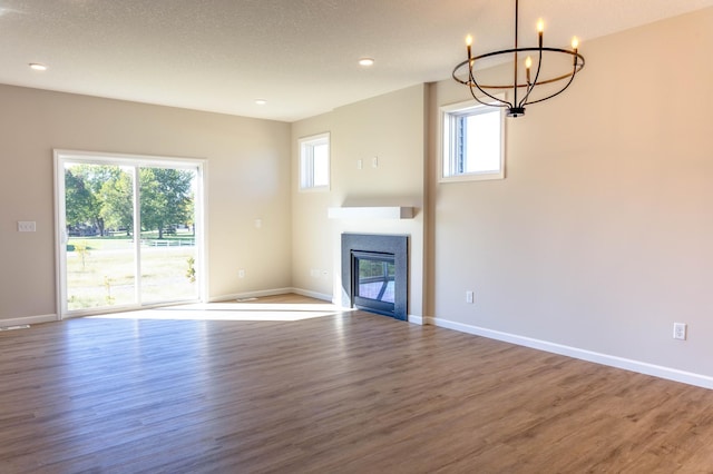 unfurnished living room featuring hardwood / wood-style floors, a textured ceiling, a wealth of natural light, and an inviting chandelier