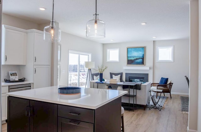 kitchen with a center island, light wood finished floors, light countertops, a glass covered fireplace, and white cabinetry