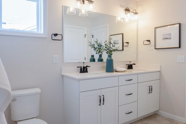 full bathroom with double vanity, a sink, toilet, and baseboards