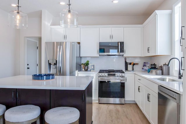 kitchen with stainless steel appliances, a sink, light countertops, decorative backsplash, and a kitchen bar