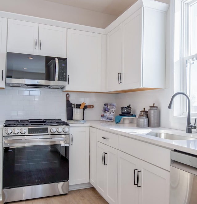 kitchen with stainless steel appliances, light countertops, decorative backsplash, white cabinetry, and a sink