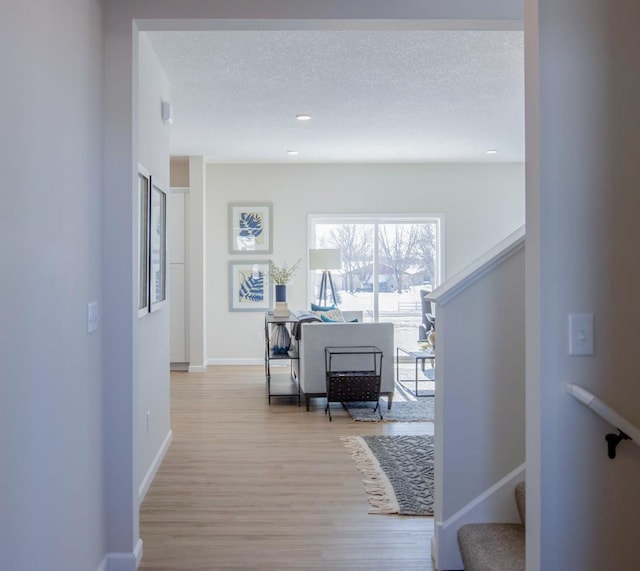 corridor featuring baseboards, wood finished floors, stairs, a textured ceiling, and recessed lighting