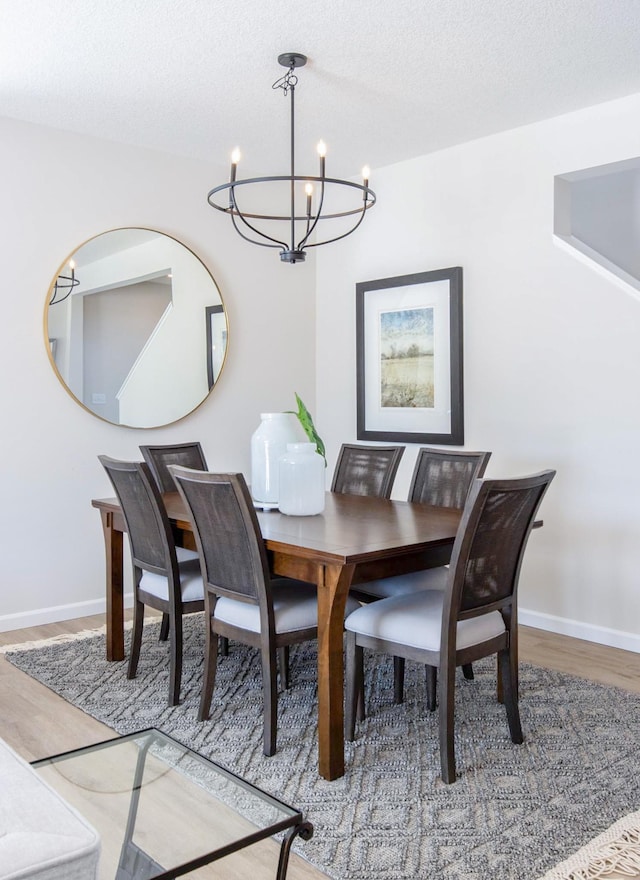 dining area with a textured ceiling, baseboards, a notable chandelier, and wood finished floors