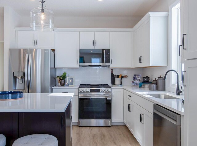 kitchen with stainless steel appliances, a sink, light countertops, light wood-type flooring, and decorative backsplash