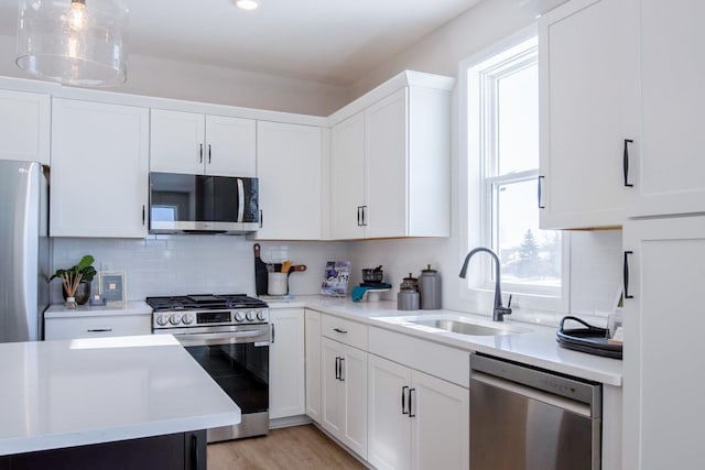 kitchen with stainless steel appliances, tasteful backsplash, light countertops, white cabinets, and a sink