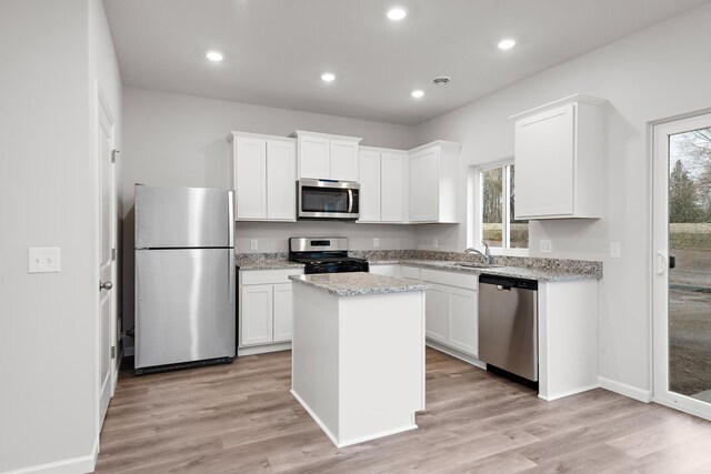 kitchen featuring white cabinets, light stone counters, a kitchen island, stainless steel appliances, and light hardwood / wood-style floors