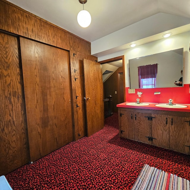 bathroom featuring vanity, lofted ceiling, and wood walls