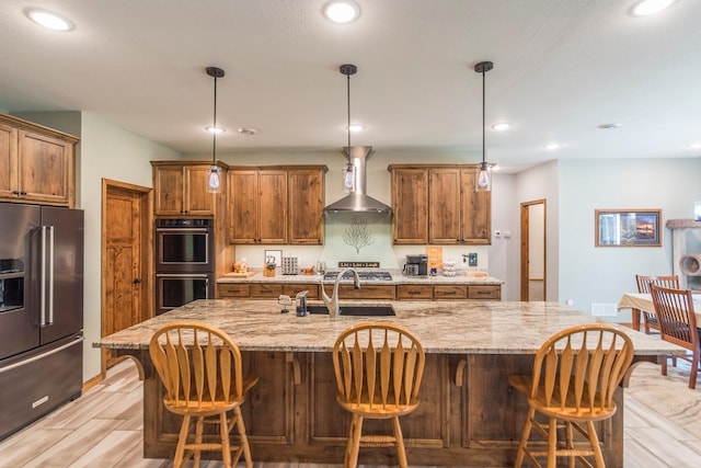 kitchen featuring light hardwood / wood-style floors, a large island, decorative light fixtures, wall chimney range hood, and black appliances