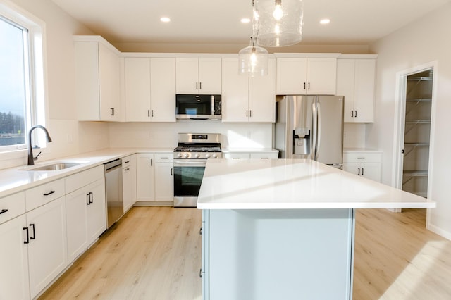 kitchen featuring sink, a kitchen island, decorative light fixtures, white cabinets, and appliances with stainless steel finishes