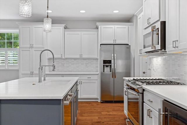 kitchen with sink, appliances with stainless steel finishes, beverage cooler, white cabinets, and pendant lighting