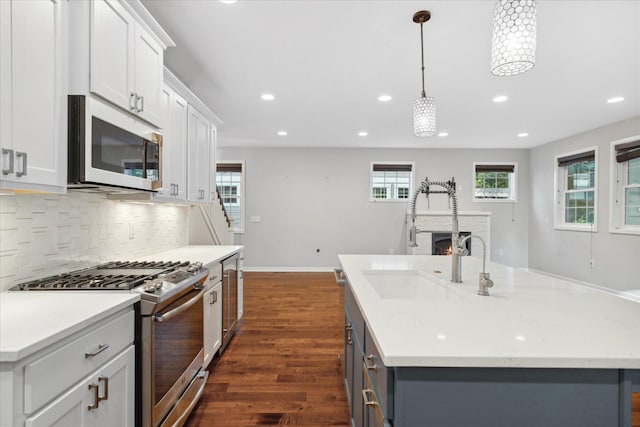 kitchen with dark wood-type flooring, white cabinets, hanging light fixtures, an island with sink, and appliances with stainless steel finishes