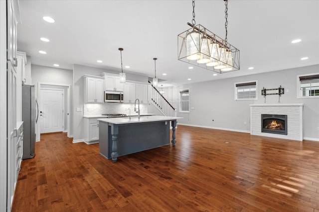 kitchen featuring a center island with sink, white cabinets, hanging light fixtures, dark hardwood / wood-style floors, and appliances with stainless steel finishes