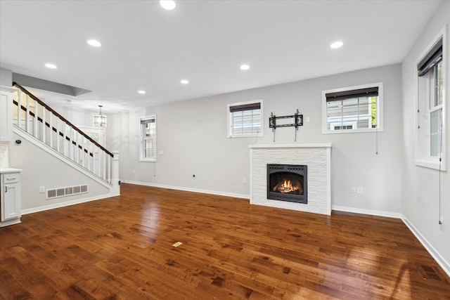 unfurnished living room with a stone fireplace, a wealth of natural light, and dark hardwood / wood-style floors