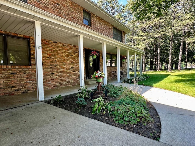 entrance to property featuring a porch, a lawn, and brick siding