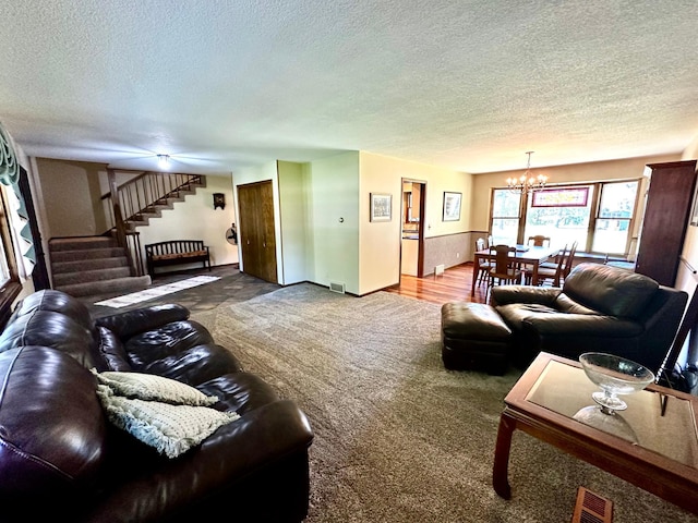 carpeted living area featuring a chandelier, visible vents, a textured ceiling, and stairs