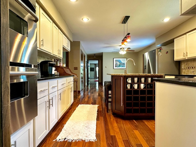 kitchen featuring dark wood-type flooring, double wall oven, white cabinetry, pendant lighting, and backsplash