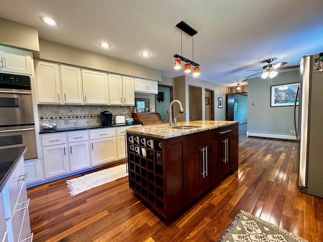 kitchen featuring an island with sink, appliances with stainless steel finishes, dark wood-type flooring, hanging light fixtures, and a sink