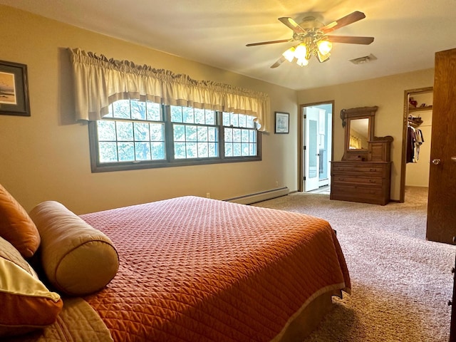 carpeted bedroom featuring a walk in closet, visible vents, a baseboard heating unit, and ceiling fan