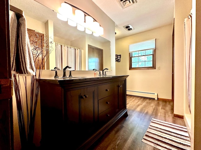 bathroom with double vanity, visible vents, wood finished floors, a baseboard heating unit, and a sink