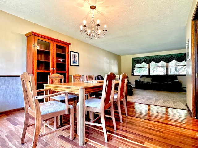 dining space featuring light wood-type flooring, a notable chandelier, and a textured ceiling