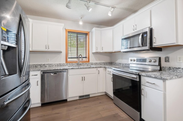 kitchen with dark wood-type flooring, sink, white cabinetry, light stone counters, and appliances with stainless steel finishes