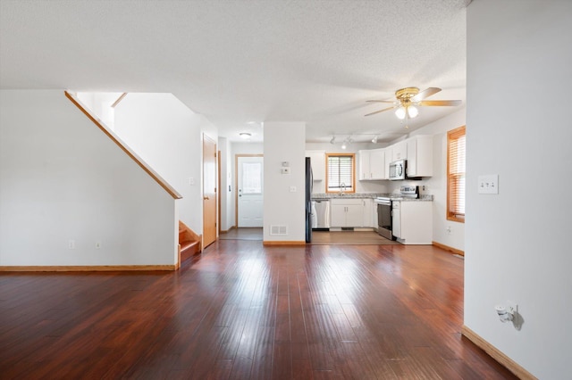 unfurnished living room with ceiling fan, dark hardwood / wood-style floors, track lighting, and a textured ceiling