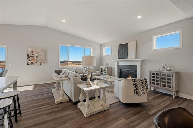 living area with a warm lit fireplace, baseboards, lofted ceiling, dark wood-style floors, and recessed lighting